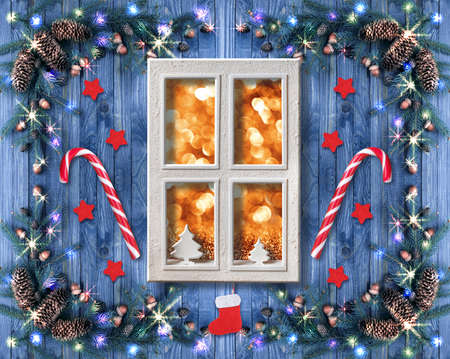 Christmas cottage window decorated with New Year decor in rustic vintage style with light illumination garland, candy cane lollipops, fir tree and spruce cones. Winter holidays interior decor concept.の写真素材