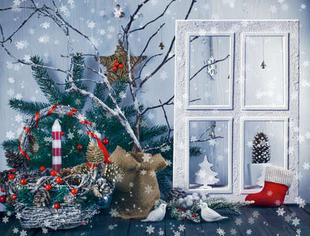 Christmas eve background with window, wicker festive basket, birds, candle, fir tree, pine, spruce cones, acorns on shabby wooden old table, New Year night winter holiday home natural material decorの写真素材
