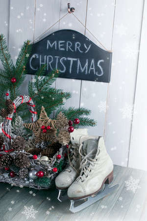 Merry Christmas background with wicker basket, skates for figure ice skating, fir tree on shabby wooden old table, blackboard with inscription on white wall, New Year holiday rustic home interior.の写真素材