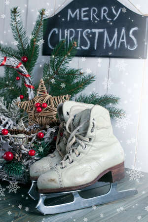 Merry Christmas background with wicker basket, skates for figure ice skating, fir tree on shabby wooden old table, blackboard with inscription on white wall, New Year holiday rustic home interior.の写真素材