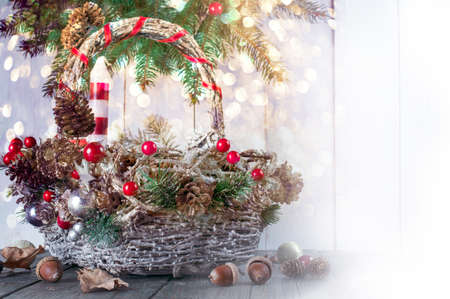 Christmas background with festive wicker basket, candle, fir tree wreath, acorns, pine and spruce cones on wooden table, New Year winter holiday home natural material decor, glowing shining bokeh.の写真素材