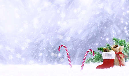 Christmas fabulous card with Santa Claus boot, gift bag, candy canes lollipops on winter snow background with snowfall and snowflakes. Fantasy new year landscape with snowy fir tree forest, copy spaceの写真素材