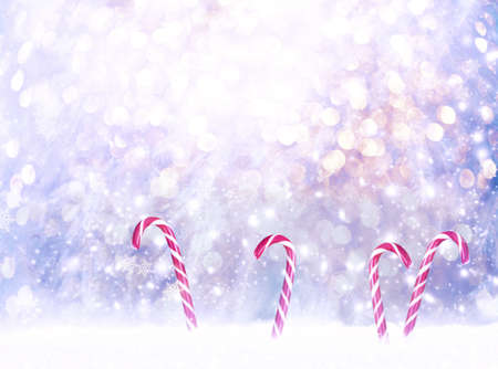 Christmas fabulous card with candy canes lollipops in snowdrift on winter snow background with snowfall, snowflakes ang glowing festive light bokeh. Fantasy new year snowy landscape with copy space.の写真素材