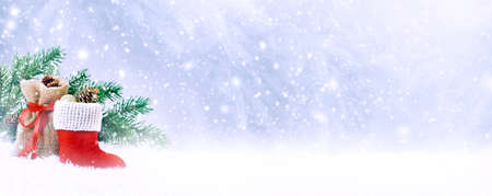 Christmas fabulous card with Santa Claus boot, gift bag and spruce branch on winter snow background with snowfall and snowflakes. Fantasy new year landscape with snowy fir tree forest, copy space.の写真素材