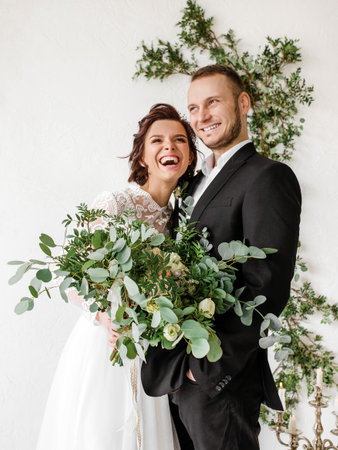 Luxury wedding couple posing in a white studio with a green leaf decorの写真素材