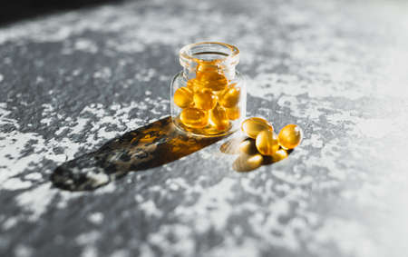 Cod liver capsules laid out in a glass bottle on a gray background.の写真素材