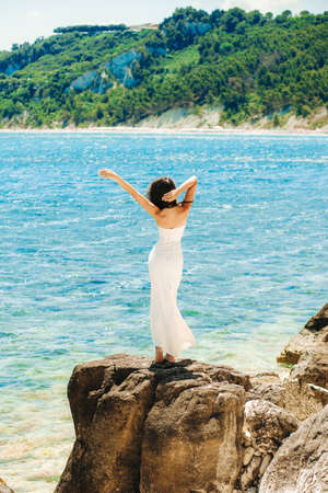 Charming girl in wedding dress standing on stone on sea backgroundの写真素材