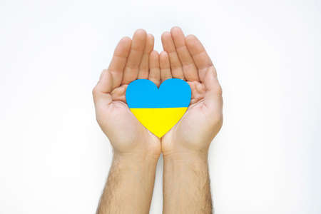 The concept of ending the war in Ukraine. Heart in the colors of the flag of Ukraine in men's handsの写真素材