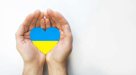 The concept of ending the war in Ukraine. Heart in the colors of the flag of Ukraine in men's handsの写真素材