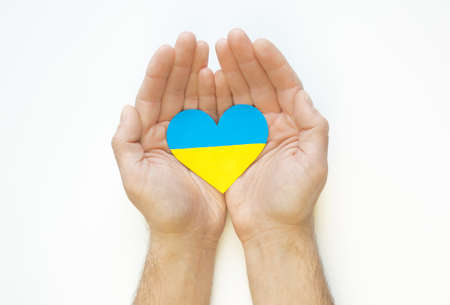 The concept of love for Ukraine. Heart in the colors of the flag of Ukraine in men's hands on a white background.の写真素材