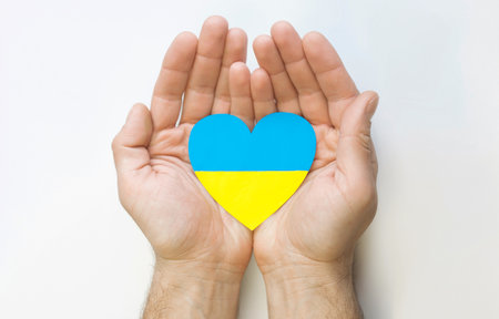 The concept of love for Ukraine. Heart in the colors of the flag of Ukraine in men's hands on a white background.の写真素材