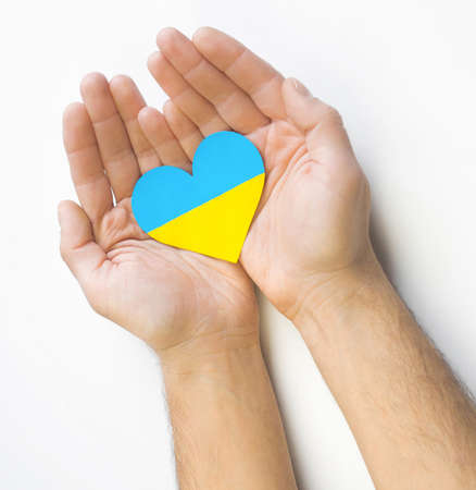The concept of love for Ukraine. Heart in the colors of the flag of Ukraine in men's hands on a white background.の写真素材