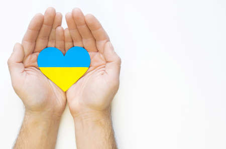 The concept of ending the war in Ukraine. Heart in the colors of the flag of Ukraine in men's handsの写真素材