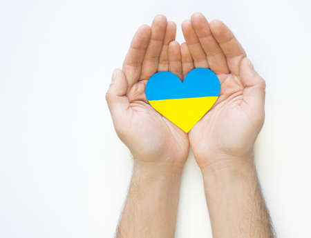 The concept of love for Ukraine. Heart in the colors of the flag of Ukraine in men's hands on a white background.の写真素材