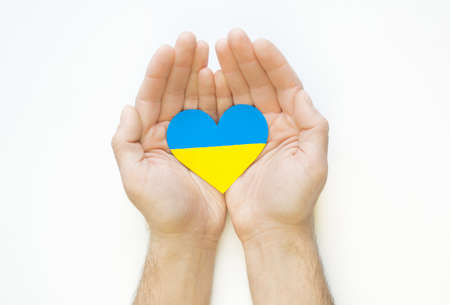 The concept of love for Ukraine. Heart in the colors of the flag of Ukraine in men's hands on a white background.の写真素材