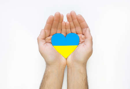 The concept of ending the war in Ukraine. Heart in the colors of the flag of Ukraine in men's handsの写真素材