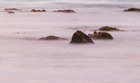 Slow shutter speed photographing water surrounding rock formation in Namibia, Africa at sunset in...