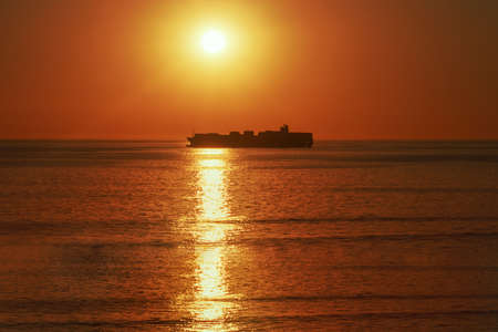 A large vessel on horizon in the atlantic ocean under the bright sun and red sunset.  Sunlight reflection off the waterの写真素材