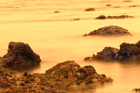 Slow shutter speed photographing water surrounding rock formation in Namibia, Africa at sunset in...