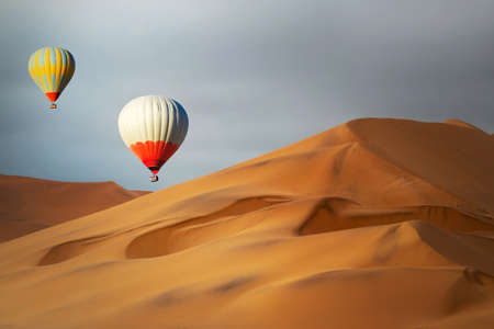 Colored hot air balloons flying over the sand dunes at sunsetの写真素材