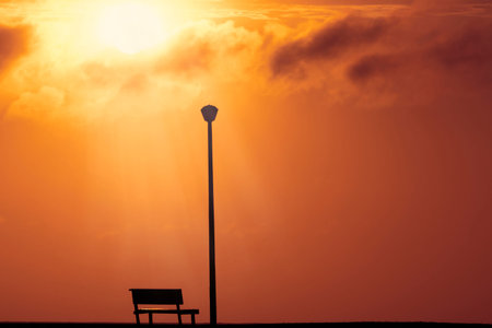 A Wooden bench and street lamp with a background view of a red sunset on sunset and a bright sun .
