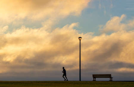 A running man,  Wooden bench and street lamp with a background view of a dramatic sunsetの写真素材