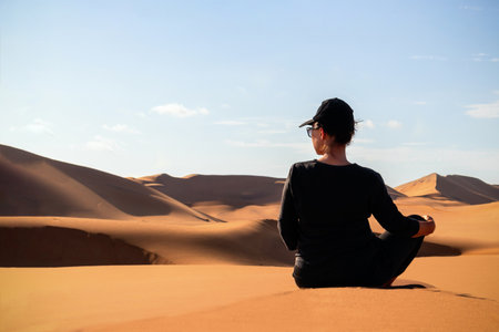 A woman is sitting on the golden sand dune of the Namib desert.の写真素材