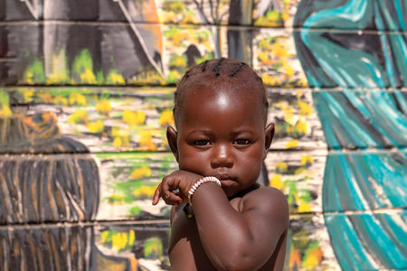 Little african black child stands near a colorful wall on a sunny day