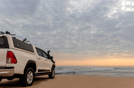 White off-road car stands on the shores of the atlantic ocean at a bright dramatic sunset