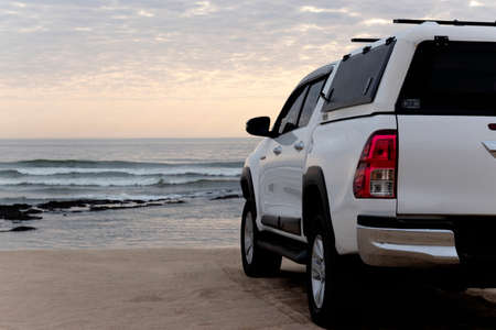 White off-road car stands on the shores of the atlantic ocean at a bright dramatic sunsetの写真素材