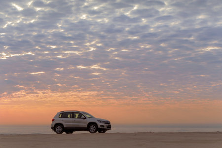Grey Volkswagen Polo stands on the coastline of the Atlantic ocean at a bright dramatic sunset