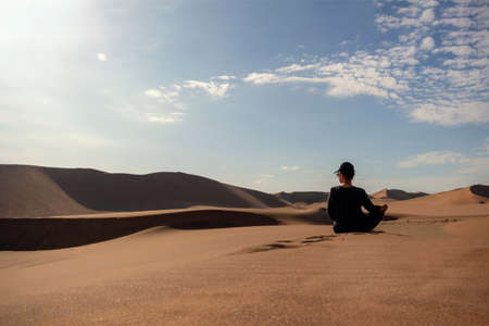 A woman is sitting on the golden sand dune of the Namib desert. Africaの写真素材
