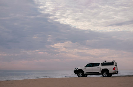 White off-road car stands on the shores of the atlantic ocean at a bright dramatic sunset