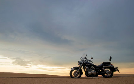 A lone motorcycle stands on the sandy surface of the Namib Desert against a dramatic cloudy sky. The...