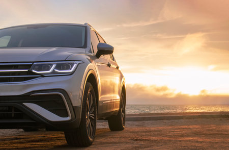 A close-up of a gray car parked on the seashore at sunset. The soft light highlights its silhouette,...