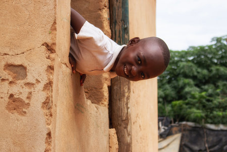 A young African boy sits quietly beside a crumbling wall in a Namibian refugee camp. A powerful image capturing the reality of displacement, strength, and human dignity.の写真素材