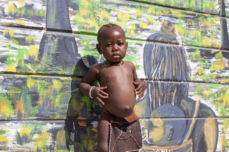 Real photo of a young African boy standing against a vivid painted wall in Namibia. A powerful...