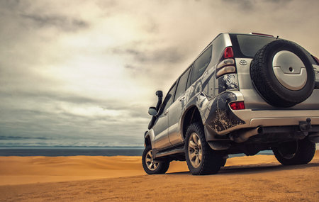 A powerful gray 4x4 SUV stands alone in the vast sandy terrain of the Namib Desert, ready for...