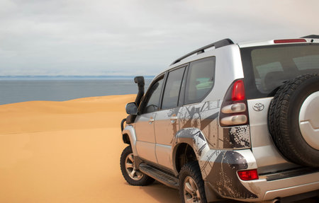 A powerful gray 4x4 SUV stands alone in the vast sandy terrain of the Namib Desert, ready for...