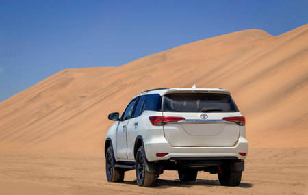 A white Toyota Fortuner parked among the golden dunes of the Namib Desert, shining under the bright summer sun. A bold symbol of off-road freedom and rugged elegance.の写真素材