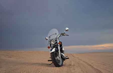 A dirt bike parked alone in the open desert, framed by stormy clouds. Perfect for themes of solitude, adrenaline, and rugged exploration on two wheels.の写真素材