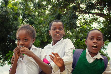 Real photo of happy black African kids in school uniforms, smiling and enjoying a break. A positive image of youth, education, diversity, and community spirit.の写真素材