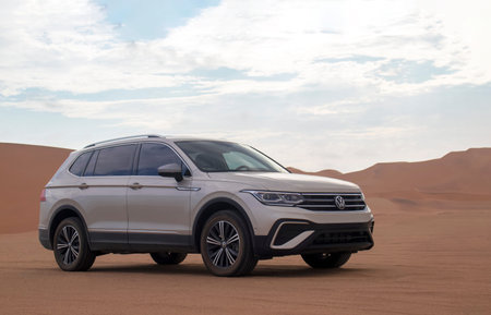 A  Volkswagen Tiguan parked amid the towering sand dunes of the Namib Desert beneath dramatic skies....