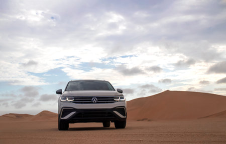 A  Volkswagen Tiguan parked amid the towering sand dunes of the Namib Desert beneath dramatic skies....
