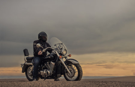Motorcyclist in desert sands during golden hour with stormy clouds above. A bold and cinematic image...