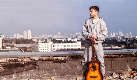 Young man on the roof of a tall building with a guitarの写真素材