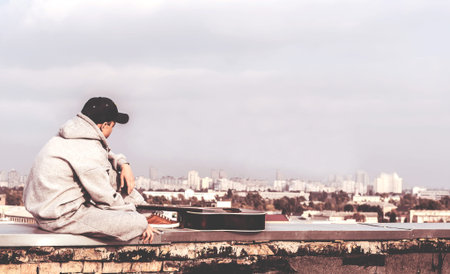 Young man on the roof of a tall building with a guitar