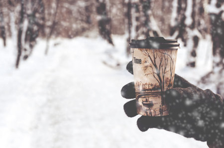 glass with hot coffee in male hand outdoors in winter