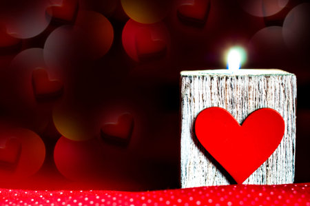Lighted candle on a beautiful red background with heartsの写真素材