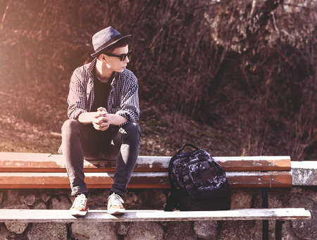 Stylish teenager sitting on a wooden bench on a city streetの写真素材